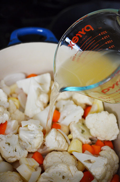 Pouring broth into the large pot with the vegetables for Roasted Garlic Autumn Root Vegetable Mash.