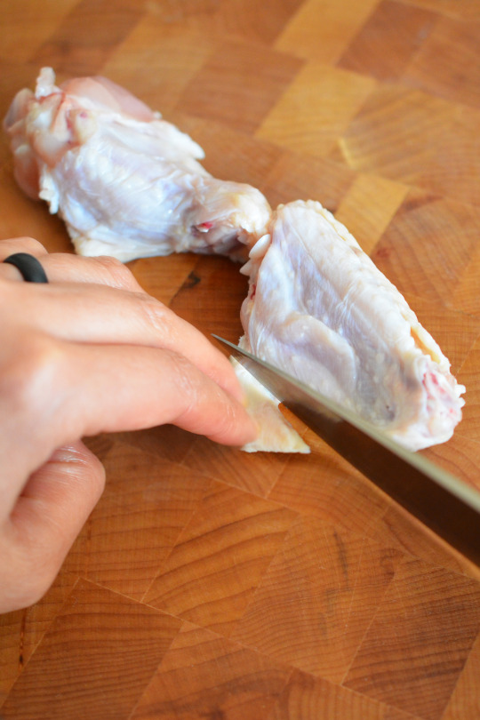 Someone trimming off the excess skin on chicken wings.