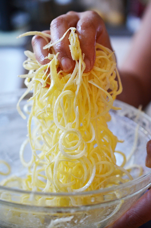 A hand grabbing a handful of spiralized sweet potatoes to make healthy Yummy Mummies for Halloween