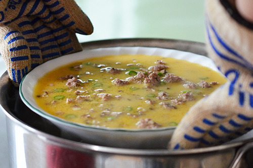 The uncooked savory egg custard is carefully placed in the pot with steaming water.