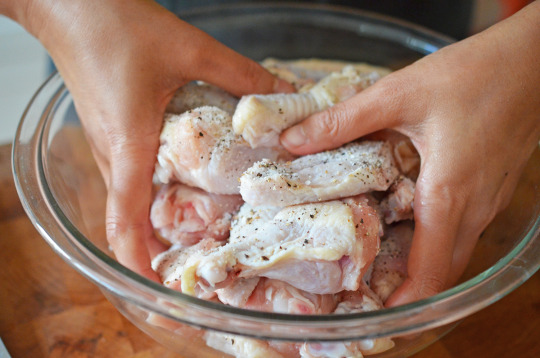 Someone tossing raw chicken wings with salt and pepper in a bowl.