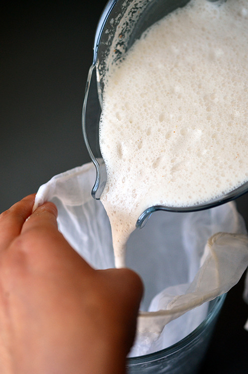 Pouring the milk mixture from the blender through the nut milk bag and into the measuring cup.