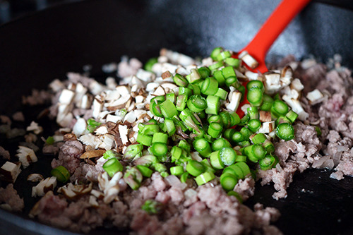 Chopped mushrooms and asparagus are added to the pan with the ground pork.