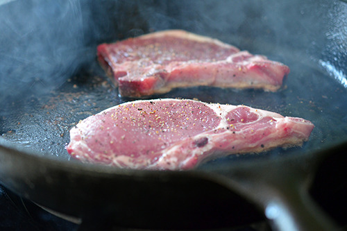 Searing off two pork chops on a cast iron skillet.
