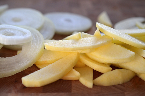 Thinly sliced onions and apples on a cutting board.