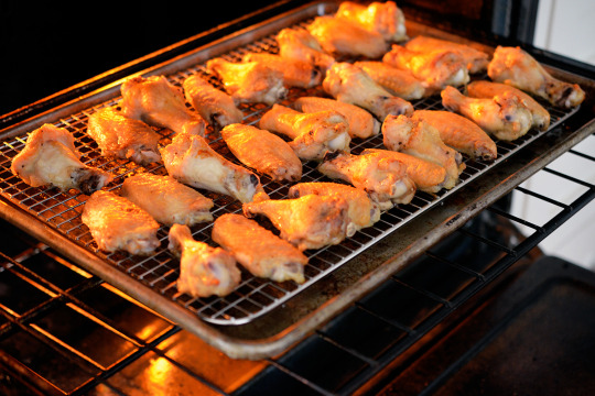 Chicken wings lined up on a wire rack being put into the oven to cook.