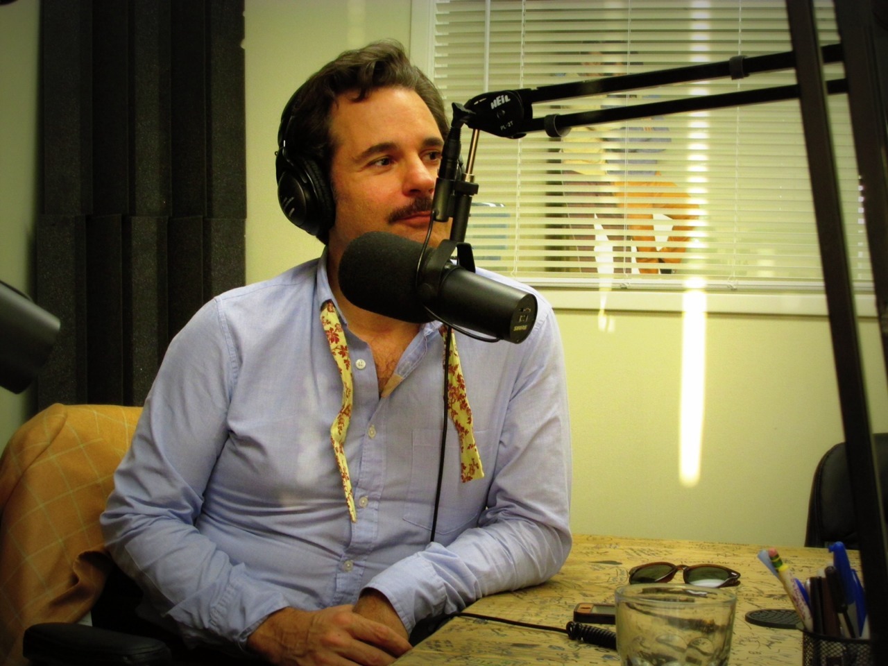 Paul F. Tompkins with an untied bowtie laughing and sitting at a microphone