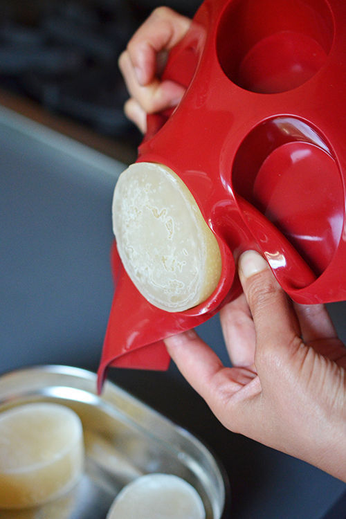 Popping out frozen bone broth pucks into a stainless steel container.
