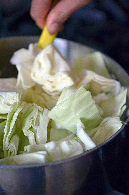 Someone stirring cabbage in a pot for ataklit ethopian vegetable stew.