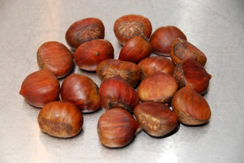 A small pile of raw chestnuts sitting on a metal countertop.