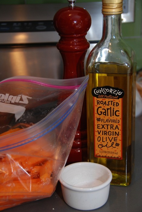 Pepper grinder, garlic extra virgin olive oil, salt, and a bag of carrots sit on a countertop.