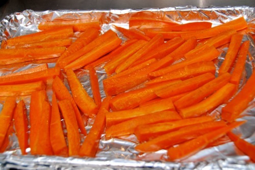 Seasoned carrots cut thin length-wise sitting on an aluminum-foil lined baking sheet.