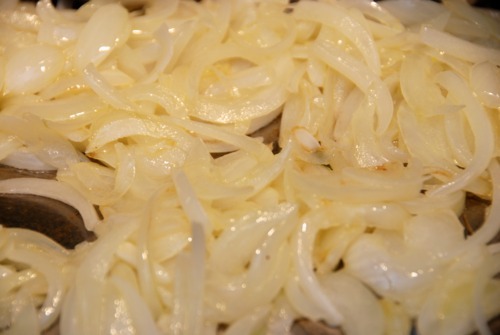 Sliced onions sautéing in ghee in a cast iron skillet.