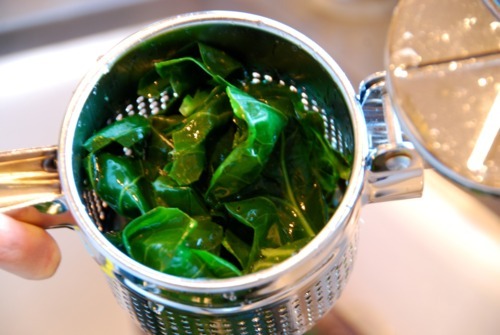 Collard greens in a potato ricer, being drained of water.