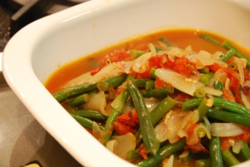 A bowl filled with paleo braised green beans with tomatoes and onions.
