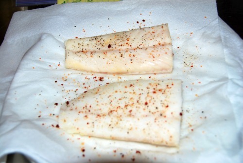 Two Alaskan cod fillets drying off on a paper towel and seasoned with black pepper and Aleppo chilé finishing salt.