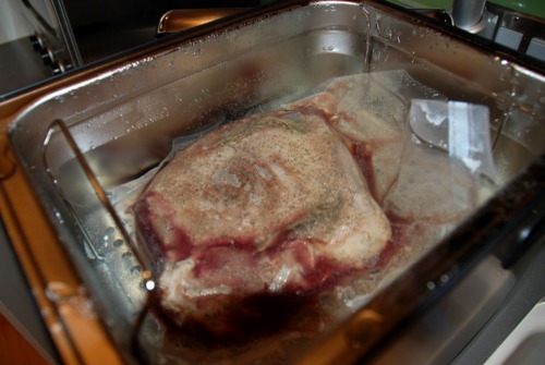 Seasoned butterflied lamb legs sitting in a sous vide machine.