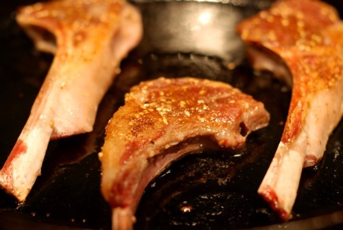 Lamb chops frying in a cast iron skillet.