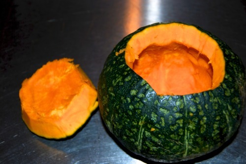 A kabocha squash with it's top cut out, revealing the inside of the squash.