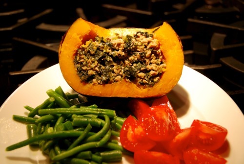 A halved pork and spinach stuffed kabocha squash with a side of green beans and tomatoes.