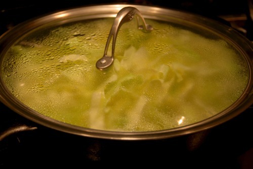 A lid covering a pan that is cooking stovetop braised cabbage.
