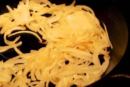 Sliced onions sautéing in a cast iron skillet.