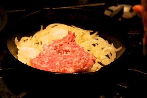 Ground pork and garlic frying in a cast iron skillet with sautéd onions.