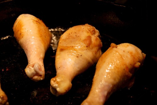 Three drumsticks frying on a cast iron skillet.