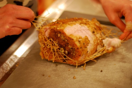Someone removing the twine on a pork leg.