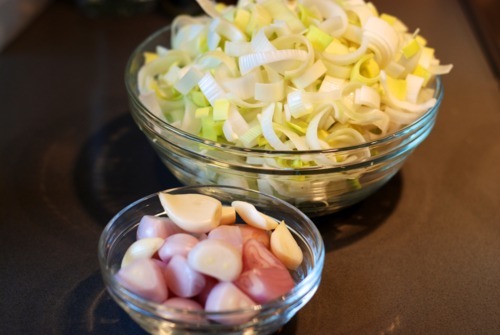 A large bowl of chopped leeks and a small bowl of shallots sitting on a kitchen countertop.