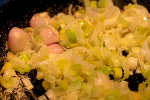 Chopped leeks and shallots frying in a cast iron skillet.