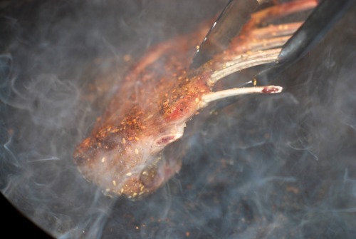 A rack of lamb being seared on a cast iron skillet.