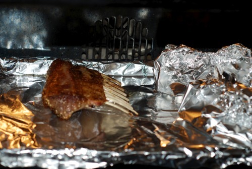 A rack of lamb being put into the oven on a foil lined baking sheet.