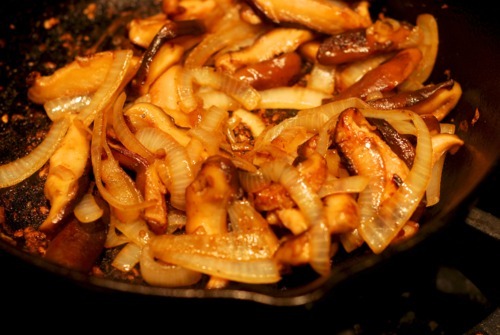 Sliced onions and shiitake mushrooms sautéing in a cast iron skillet.