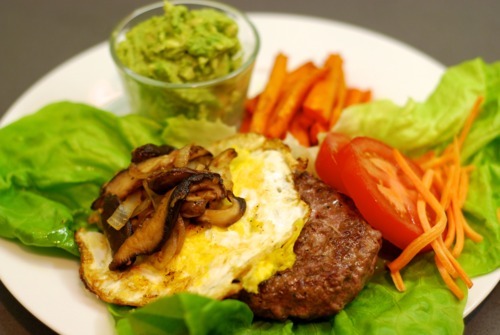 Lamb burger on a bed of lettuce topped with a fried egg and sautéed shiitake mushrooms and onions.