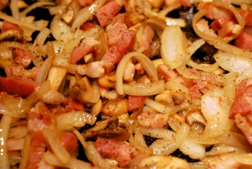 A bacon and onion mix that is being fried in cast iron skillet is seasoned with salt and pepper.