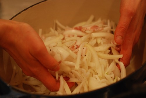 Someone mixing chopped onions in a Dutch oven. 