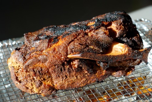 A cooked pork shoulder roast resting on a wire cooling rack.