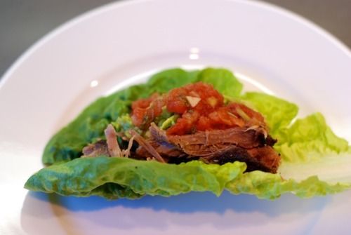 A butter lettuce leaf holding shredded oven-braised pork topped with salsa.