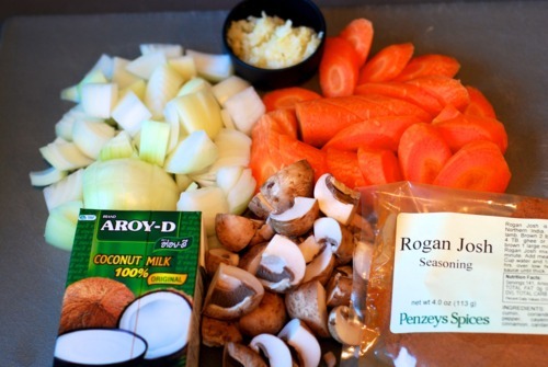 Chopped onion, carrots, garlic, mushrooms, coconut milk, and Rogan Josh seasoning all sitting on a counter.