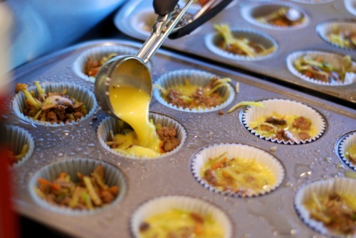 Someone is pouring whipped eggs into the cupcake tins to make muffin frittatas.