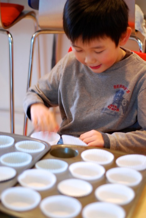 A little boy placing cupcake liners in the cupcake trays to make muffin frittatas.