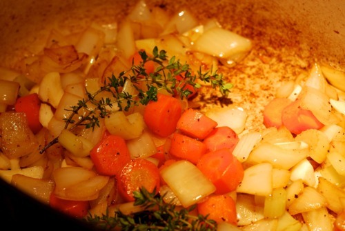 The bottom of a dutch oven with onion, carrots, garlic, and thyme being sauteed.