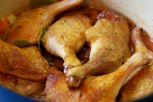 Duck legs are on top of a vegetable sauté filled with chicken broth in a dutch oven.