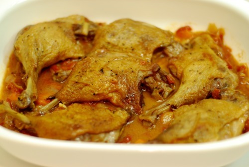 The crispy braised duck legs are resting in a white container in its duck juices.