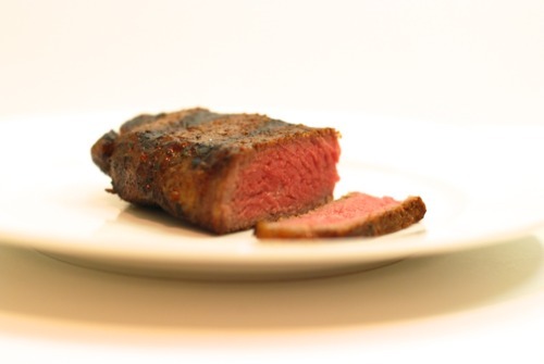 A piece of grass fed t-bone steak. One slice is cut off and you can see that the inside of the steak is pink.