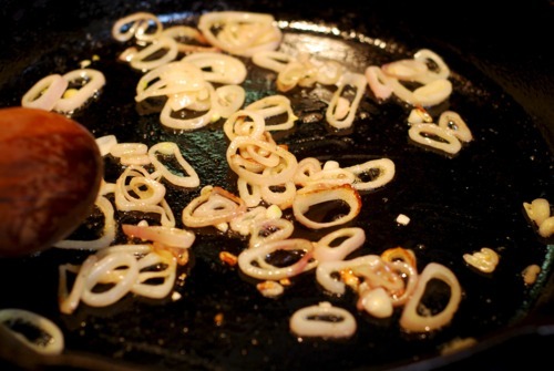 Shallots frying in a cast iron skillet with a wooden spoon.