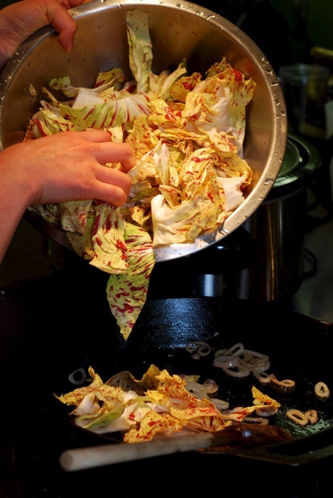 Someone is adding a bowl of chopped Castelfranco radicchio to a cast iron pan that has fried shallots.