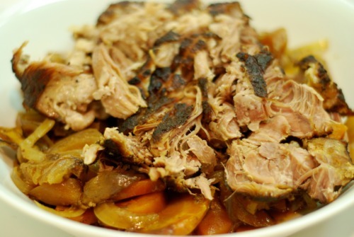 A bowl of shredded pork shoulder roast on top of carrots and onions.
