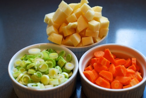 Three ramekin bowls. One is filled with sliced green onions, one is filled with cubed turnips, and one is filled with chopped carrots.